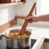 Hand holding a 12-inch acacia wood spatula for flipping burgers in a non-stick pan