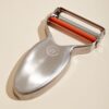 The Milk Street precision peeler in use, showing the pivoting blade navigating a curved vegetable surface.